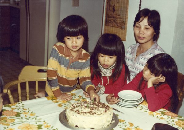 Members of the Nguyen family gather around Mary Nguyen as she inhales deeply to blow out candles on her birthday cake. From left to right are: Charlie, Mary, Hong and Thuy.