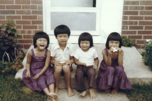 The children of Hong and Trong Nguyen sitting on the stoop outside their house. From left to right are Mary, Minh, Charlie, and Thuy, who is eating a sandwich.