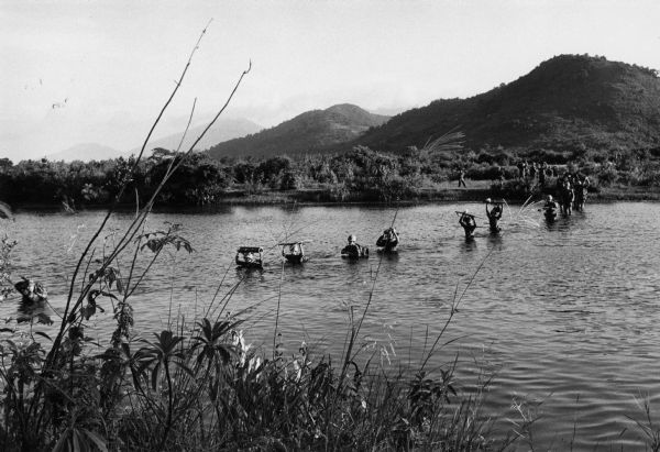 View from shoreline of U.S. Marines wading across a river while on a "Search and Clear" operation near Da Nang in Vietnam.