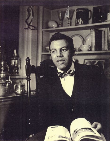 Ted Pierce dressed in formal attire, including bow tie and sitting in front of a bookcase with a book on his lap.