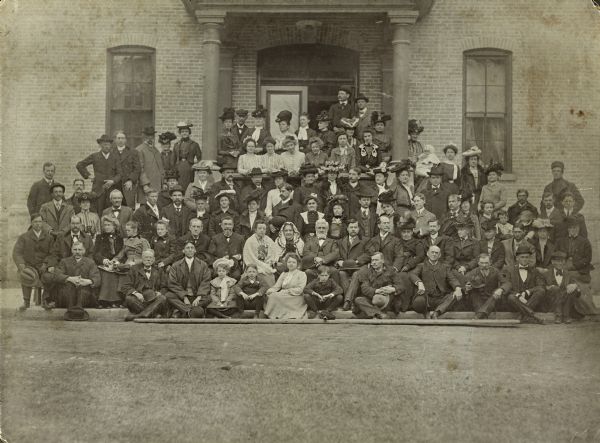 Group portrait taken at the 50th anniversary of the Wisconsin School for the Deaf, entitled "Semi-Centennial Visitors". Identified are: second from left in front row, Fred Larsen, instructor in the print shop; eighth from left in second row, Almira Hobart, wearing a shawl, teacher in the literary department; tenth from left in second row, William Lyon, President, State Board of Control; next to Lyon is C.P. Cary, Superintendent, Wisconsin School for the Deaf; next to Cary is E.M. Gallaudet, President of Gallaudet University.