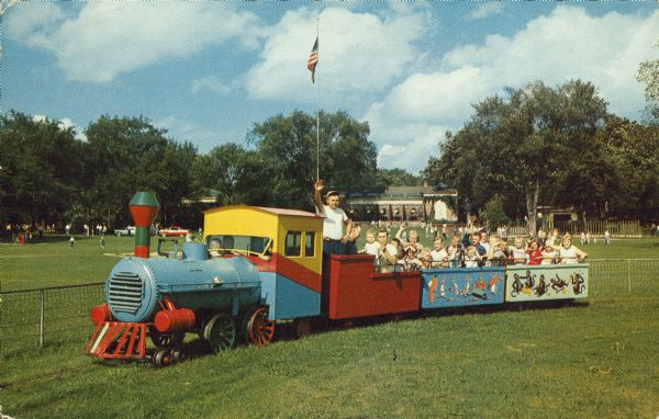 Colorful locomotive pulling several cars full of children at the Vilas Park Zoo (Henry Vilas Zoo). Although referred to as the "Kiddie Train," the caption notes it was a train for "children of all ages." It was donated by the Madison Lions Club and operated between 1953 and 1968.