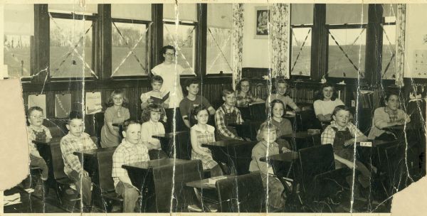 Teacher and students. The students are posed seated at their desks inside the school. The teacher is Mrs. Rose Chitwood.