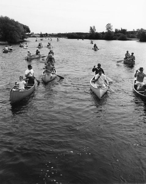 Large group of people in canoes on a river.

