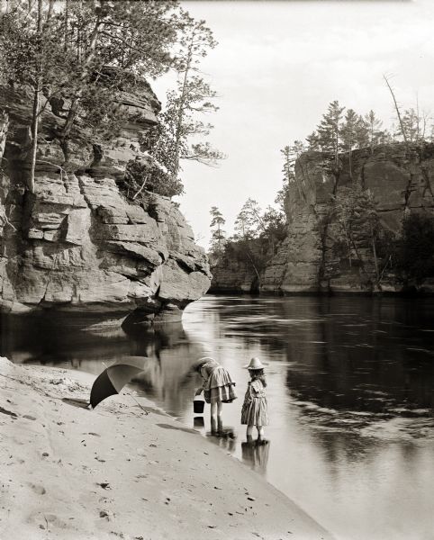 View down sandy beach towards Miriam and Ruth Bennett wading in river near Romance Cliff at a sand bar above High Rock.