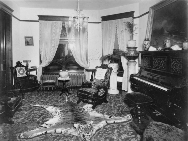 An interior view of the Halle Steensland house at 315 North Carroll Street, showing the lavishly decorated parlor. There is a piano on the right, and a tiger rug on the floor.