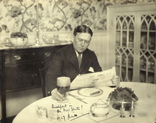 H.L. Mencken sits at the breakfast table reading the newspaper and dining on toast and a goblet of beer. He autographed the photograph with "Breakfast in the Free State!" and his signature.