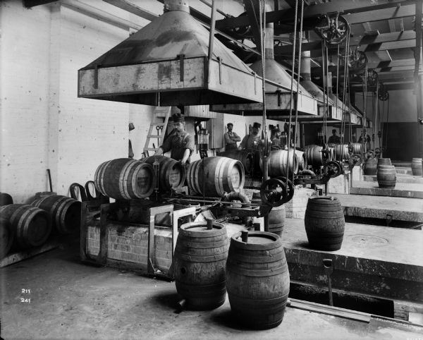 Interior view of Pawling & Harnischfeger hoist cranes in a Schlitz brewery where men are working with beer barrels.