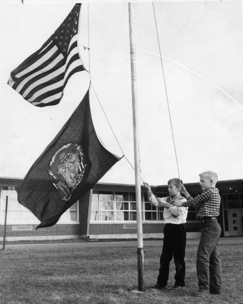 Two boys raise the United States and Wisconsin flags in front of their Rock County school.