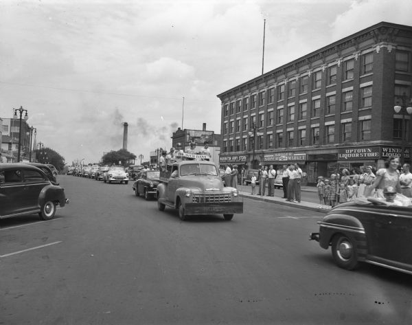 Soap Box Derby Parade of Youth showing the Beaver Dam float and those from nearby communities. The Uptown Liquor Store and other businesses along the 100 block of East Washington Avenue are in the background.