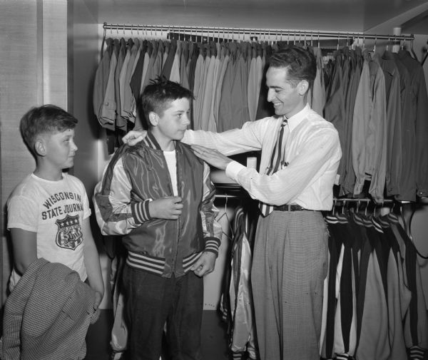 Phil Lenhart and Warren Slightam, Soap Box Derby winners, are awarded sports jackets (letterman jackets) by Johnny Casey, manager of the boys' department at Olson and Veerhusen's clothing store.