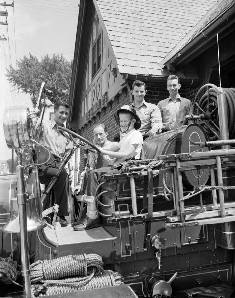 Soap Box Derby Entrant, 11-year-old Johnny Huseboe, behind the wheel of a fire truck at No. 5 fire station, 2137 Atwood Avenue, along with four fire fighters. Johnny is being sponsored in the race by Local 311 of the Fire Fighters union. Pictured from left to right are: Charles Merkle, Harold Dennis, Johnny Huseboe, Jim McAusland, and Kermit "Hermy" Hermanson, president of the Madison Fire Fighters local.