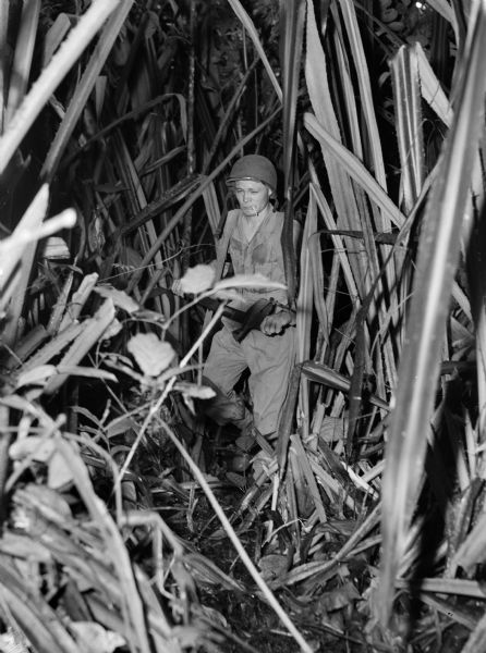 A soldier hacks a path through a jungle in Panama with a machete while smoking a cigarette.