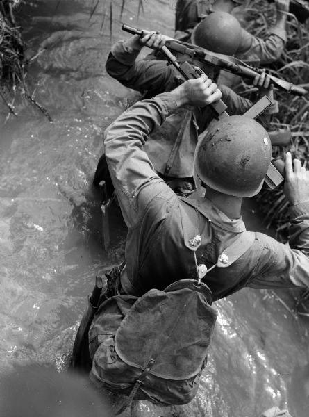 Rear view of soldiers holding their rifles above their heads as they ford a stream in Panama.