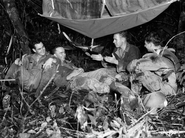 Four soldiers are seated under a canopy in Panama, relaxing and talking.
