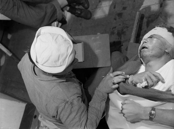 A badly wounded Marine suffers with an abdominal injury in Iwo Jima. A medic is sitting near him checking his identification tag.