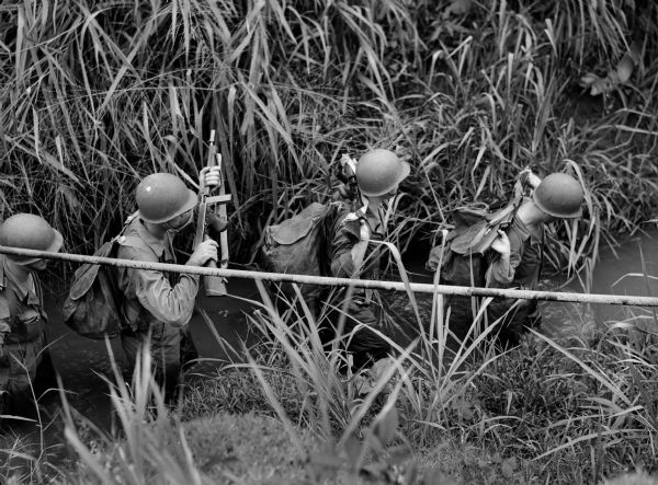 Soldiers fording a stream in Panama holding rifles high.
