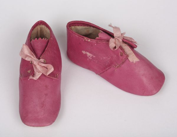 A pair of bright pink, leather baby shoes with pale pink ribbons, made in 1851.