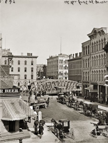 Elevated view of Grand Avenue. A number of horse-drawn carriages are lined up near a bridge.