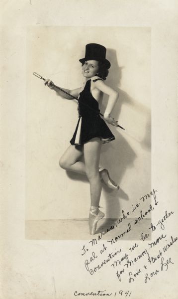 Portrait of Lora Lee holding a cane and wearing a top hat, dancing costume and ballet shoes. It is inscribed "To Marian, who is my pal at Normal School & convention. May we be to-gether for Many More. Love & Best Wishes, Lora Lee".