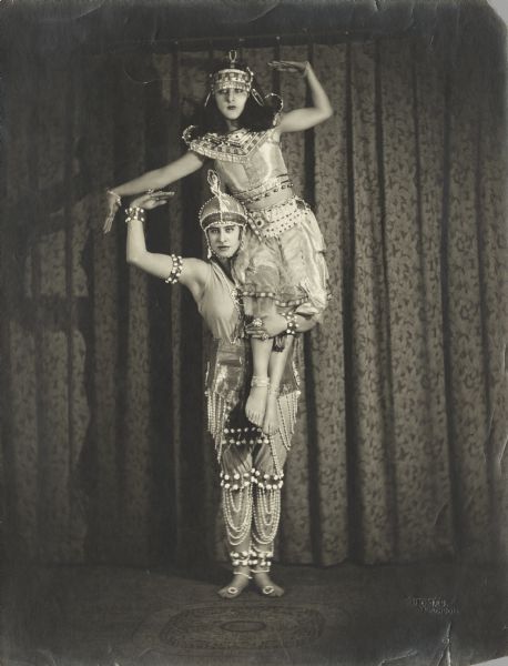 Billie Sidell, dressed as a man, poses with her sister, Pierre Sidell, who is sitting on her shoulder. They are wearing elaborate, ornate costumes.