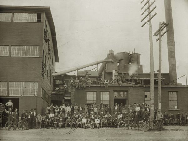 Men posed in front of and on top of a building at Plant One of the Curtis and Yale Co. Some of the men stand with bicycles.