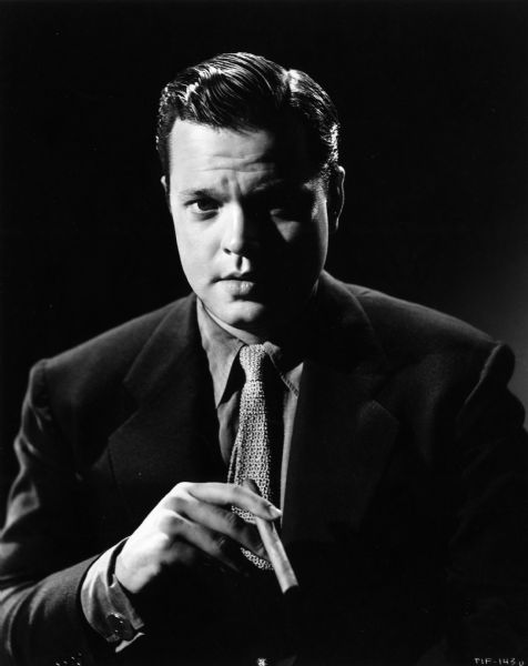 A dramatic, glamorous portrait of a young Orson Welles holding a cigar.