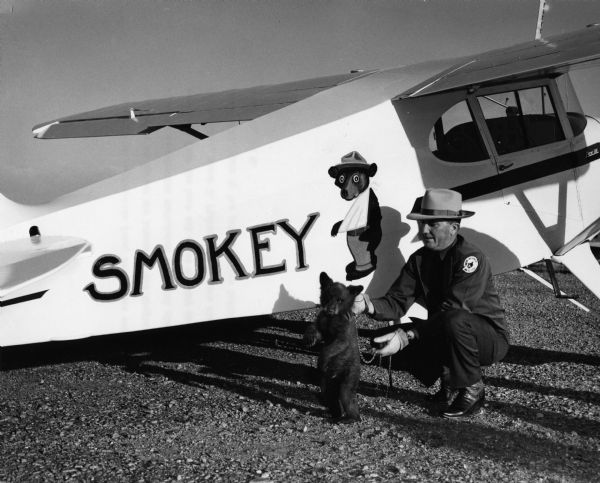 Smokey Bear cub and his handler, Homer C. Pickens, pose by a Piper Aircraft Corporation airplane named in Smokey's honor prior to flying to Washington, D.C.