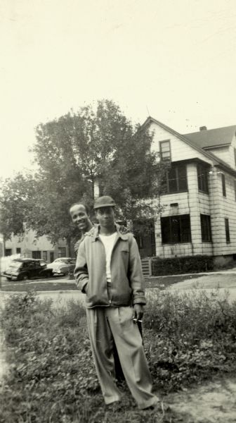 Lewis Arms peeks from behind Jerome Williams, who is holding a cigarette. They are standing outdoors near a street.