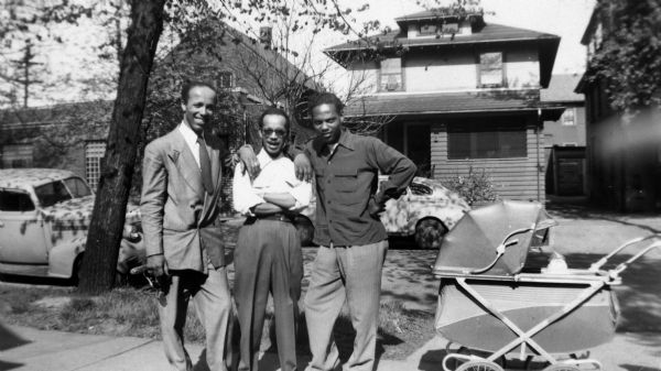 Three men from the Arms family pose together on a sidewalk on Frances Street. From left to right are Lewis Arms, Wilbur Arms and Eddie Arms. There is a baby carriage next to Eddie.