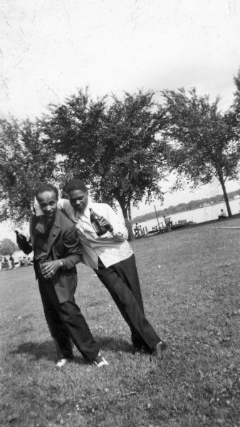 Lewis Arms and a friend, looking dapper in their suits, pose together at Brittingham Park. They're holding bottles and goofing around.