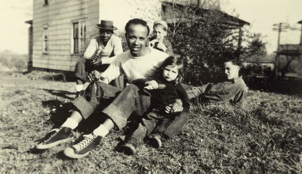 Lewis Arms and Bert Rogers sit on a lawn with three children. Some of them are eating popsicles.