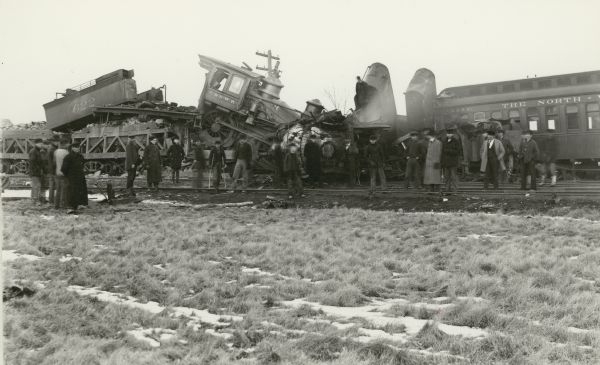 A crowd of men gather around a wrecked Chicago and North-Western train.