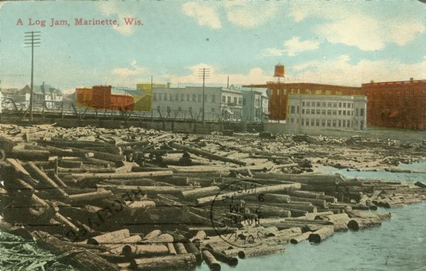 Colorized view of a log jam scene with industrial buildings in the background. Caption reads: "A Log Jam, Marinette, Wis."