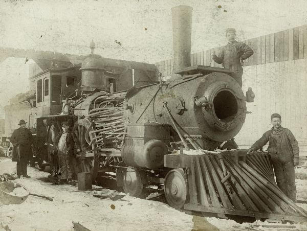 Four men pose next to a locomotive, which has a hole in its side due to an explosion.