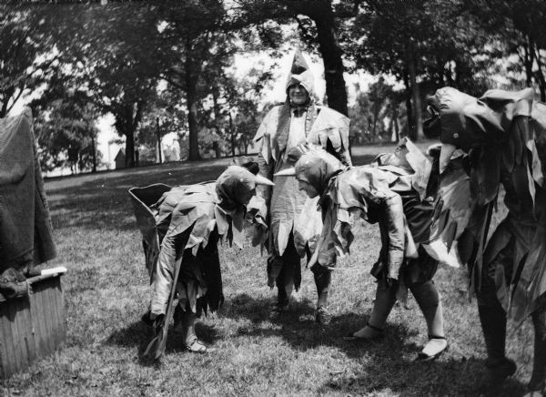 Four costumed Rockford College students pose outdoors in mock battle on a lawn. Fighting roosters [?].