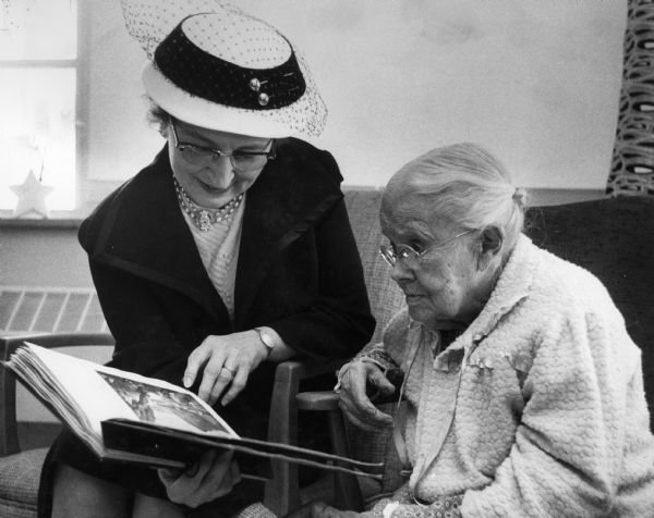 A fashionably dressed woman is sharing a book with an elderly woman.