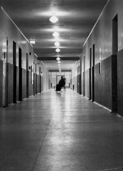 A view down a hallway at the Dane County Hospital and Home, with the silhouette of a man in a wheelchair at the end.