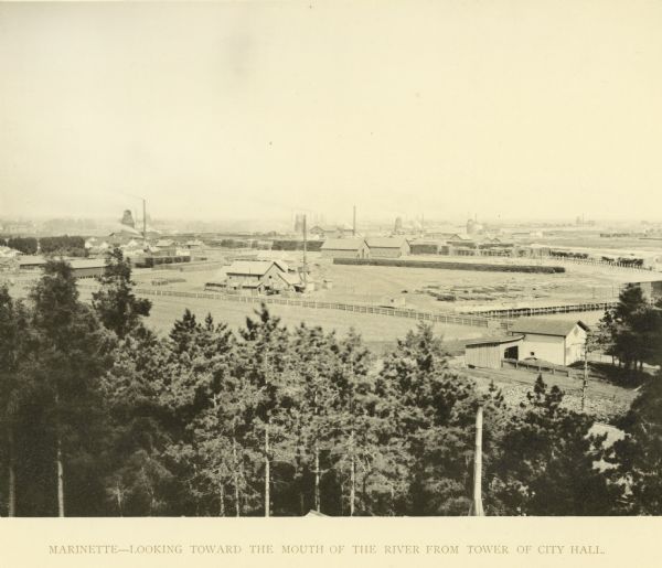 Elevated view of Marinette looking toward the mouth of the river from the tower of City Hall. Fences, fields, and industrial buildings are in the foreground.