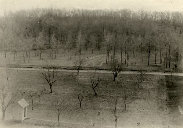 Elevated view of Man Mound outlined in chalk looking south. A road bisects the legs of the effigy mound. A small outbuilding can be seen at left in the foreground.