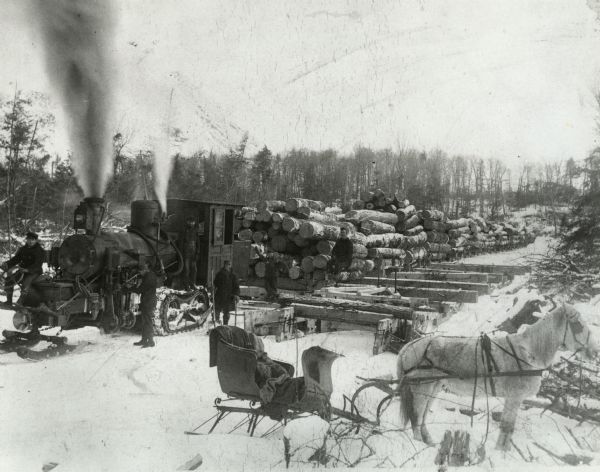 Lumber crew posed with a steam hauler and several sleds loaded with logs. The foreman's sleigh pulled by a horse is in the foreground. Possibly foreman, Mike Baltus, at the head of the steam hauler.