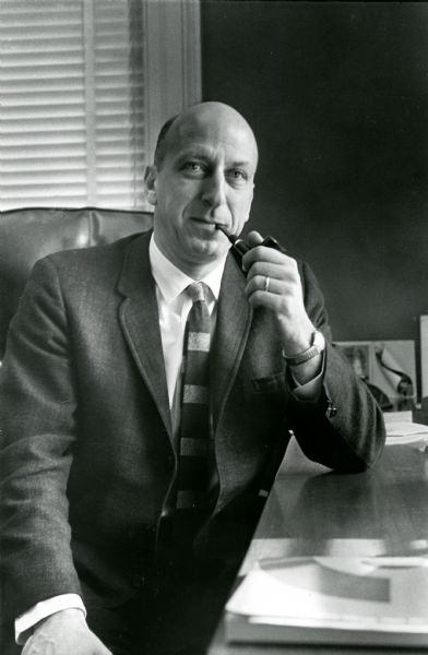 Portrait of Leslie H. Fishel, Jr., holding a pipe and sitting at a desk. He was the Director of the State Historical Society of Wisconsin from 1959 until 1969.