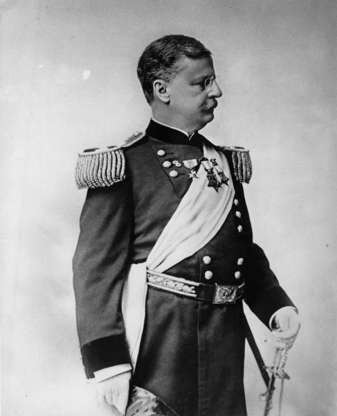 Three-quarter length portrait of Major General Arthur MacArthur in profile, wearing a military uniform and holding a sword, and a hat.