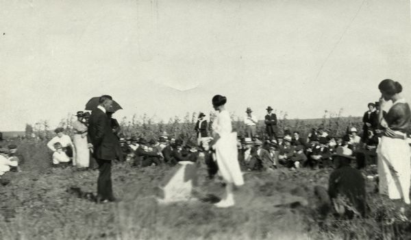 Anna Fox, great-grand niece of Ebenezer Brigham, just after removing the flag unveiling the bronze tablet commemorating Fort Blue Mounds. State historical Society of Wisconsin Director, Joseph Schafer, reads the text of the tablet at the close of the unveiling address. Several onlookers are seated or stand in the background.