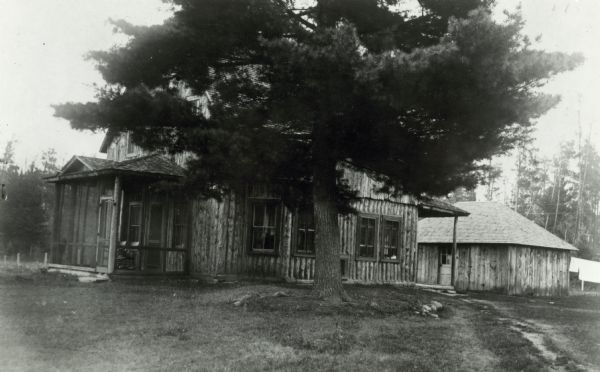 Exterior view of Joe Lucius's cottage on the Brule River. There is a huge pine tree in front of the cottage. The first seedlings were taken from this tree for reforestation in Wisconsin.