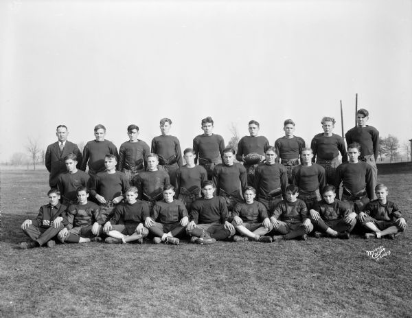 Outdoor team portrait of the Middleton High School Football Squad in uniform. One of the boys in the center standing at the back is holding a football with writing that reads: "Champs 1930."