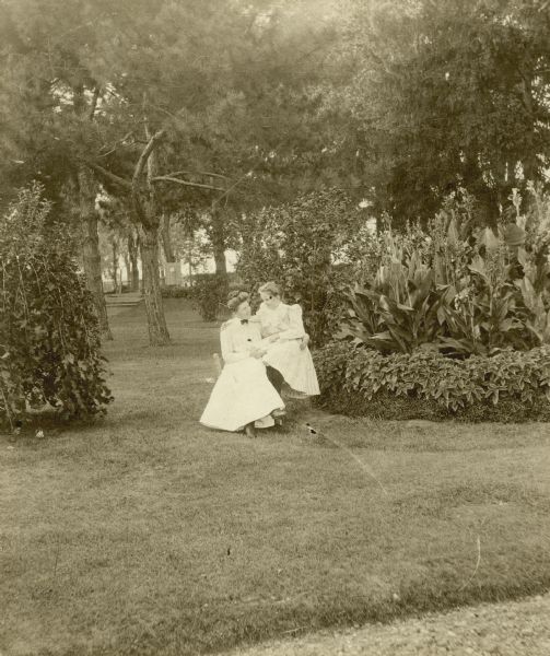 Violet and Judith Dousman seated together between a canna bed and a weeping mulberry.