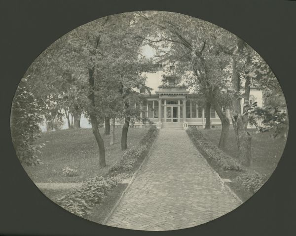 View along the path leading to the east entrance at Villa Louis. The herringbone pattered brick path is lined with trees and coleus plants.