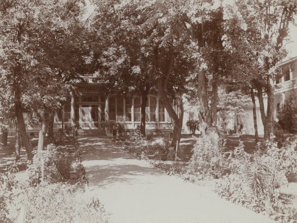 View of the East Walkway at Villa Louis. The walk is lined with trees and flower beds.