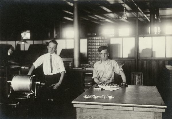 A man teaches a boy practical printing with large type in a proof press at Western Printing Company.